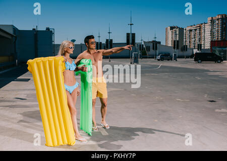 Happy young couple en vêtements de plage avec lits gonflables sur le stationnement Banque D'Images