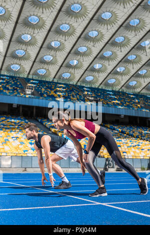 Fit young sprinters masculins et féminins en position de démarrage sur une piste de course au stade de sport Banque D'Images