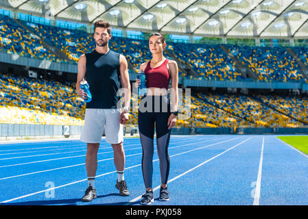 Jeune couple sportif avec des bouteilles d'eau de vous détendre sur une piste de course au stade de sport Banque D'Images
