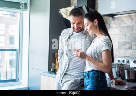 Smiling couple using smartphone together in kitchen, smart home concept Banque D'Images