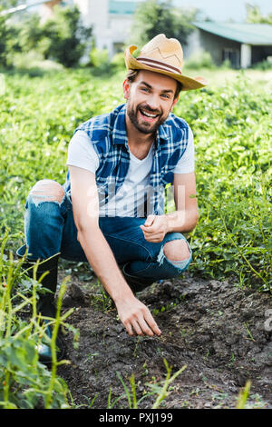 Happy handsome agriculteur planter les graines de citrouille dans le champ au niveau de l'exploitation Banque D'Images