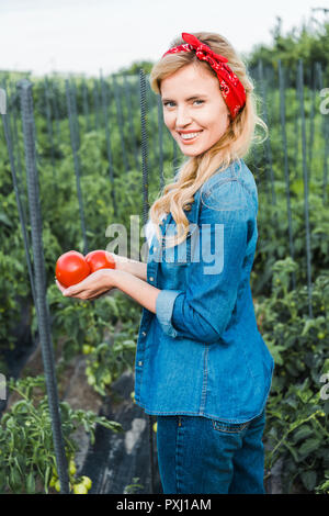 Belle farmer holding venu les tomates biologiques dans le champ au niveau de l'exploitation Banque D'Images