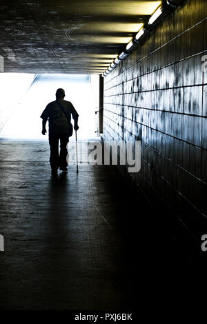 Silhouette d'un homme marchant avec un bâton dans un passage inférieur Banque D'Images