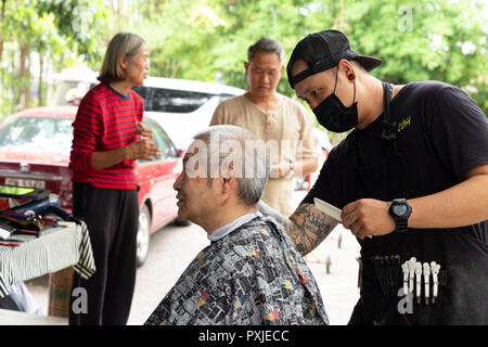 Un artisan homme coiffure couper les cheveux d'un vieil homme à JingJai Farmer's Market, Chiang Mai, Thaïlande Banque D'Images