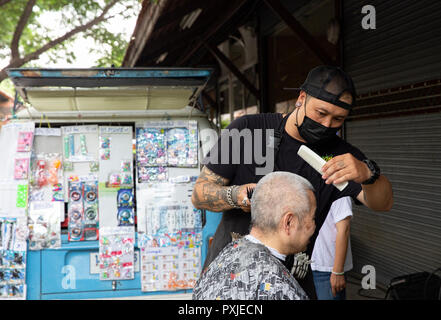 Un artisan homme coiffure couper les cheveux d'un vieil homme à JingJai Farmer's Market, Chiang Mai, Thaïlande Banque D'Images