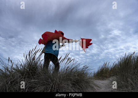 Homme portant un manteau de pluie imperméable rouge luttant avec un parapluie par temps venteux. Banque D'Images