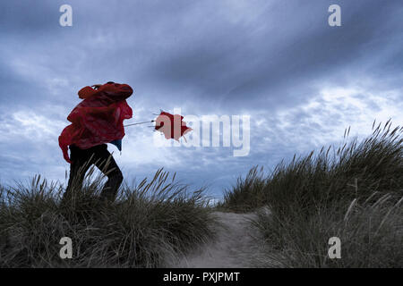 Homme portant un manteau de pluie imperméable rouge luttant avec un parapluie par temps venteux. Banque D'Images