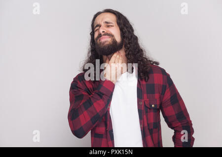 Portrait d'un bel homme avec barbe et cheveux longs noirs dans un style décontracté, chemise rouge à carreaux avec douleur permanent sur son cou et ferma les yeux Banque D'Images