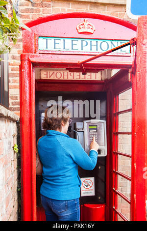 Chat femme parle à l'aide d'un téléphone dans une cabine téléphonique anglaise rouge traditionnel design kiosque no 6 / K6 conçu en 1935 par Sir Gilbert Scott Banque D'Images