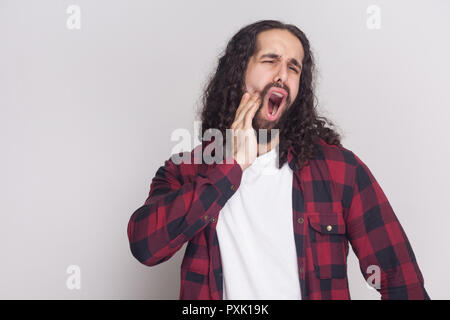 Triste crier bel homme avec barbe et cheveux longs noirs dans un style décontracté, chemise rouge à carreaux avec dents douloureux permanent et se sentir mal de dents Banque D'Images
