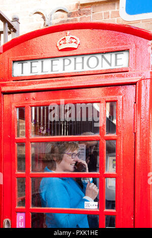 Chat femme parle à l'aide d'un téléphone dans une cabine téléphonique anglaise rouge traditionnel design kiosque no 6 / K6 conçu en 1935 par Sir Gilbert Scott Banque D'Images