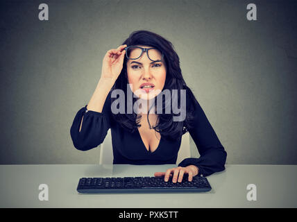 Jeune femme d'affaires à l'aide du clavier et les yeux plissés ayant des problèmes de vision sur fond gris Banque D'Images