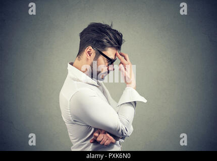 Vue latérale du barbu à lunettes et une chemise blanche touching forehead étant en dépression et pleine de pensées Banque D'Images