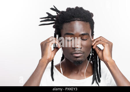 Homme teint foncé avec des dreadlocks à l'écoute de la musique sur le casque Banque D'Images