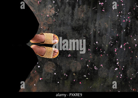 Vue sur la grande scène avec pieds de femme porter un pantalon noir et des sandales en plastique jaune en stand-de-chaussée avec petit jardin à la chute des pétales de fleurs Banque D'Images