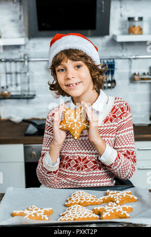 Happy cute boy in santa hat holding de délicieux biscuits au gingembre et smiling at camera Banque D'Images