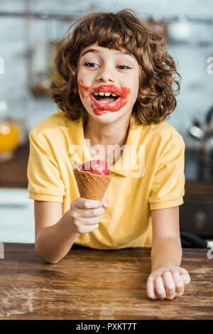 Adorable happy boy avec de la glace sur le visage délicieux holding ice cream cone Banque D'Images