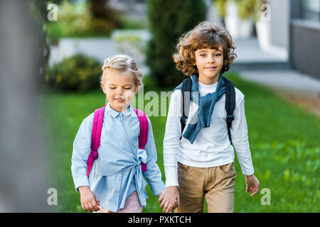 Adorable little schoolkids holding hands sur pelouse verte Banque D'Images