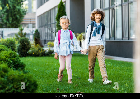 Adorable schoolkids with Backpacks holding hands sur pelouse verte Banque D'Images