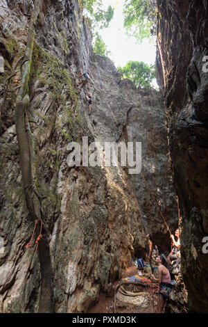 Groupe de touristes haut de la corde et dans un canyon étroit et raide avec deux grands visages de calcaire qui est un site d'escalade à Vang Vieng Banque D'Images
