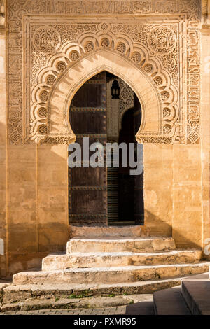 Façade en pierre traditionnelle de l'entrée de la mosquée, avec une porte ouverte en bois. Quelques marches de la rue. La lumière du soleil du matin. Rabat - Maroc, Vente Banque D'Images