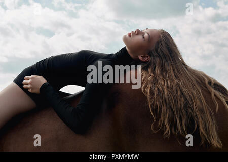 Girl-cavalier se trouve sur un cheval dans le champ. Fashion portrait d'une femme et les juments sont des chevaux dans le village dans le ciel. Femme blonde et c'est dr Banque D'Images