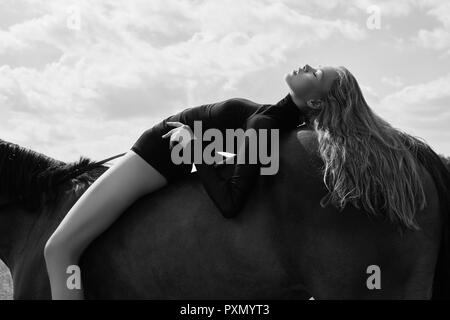 Girl-cavalier se trouve sur un cheval dans le champ. Fashion portrait d'une femme et les juments sont des chevaux dans le village dans le ciel. Femme blonde et c'est dr Banque D'Images