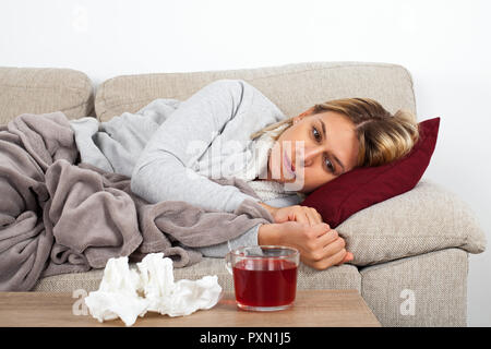 Jeune femme ayant la grippe saisonnière est en appui sur thesofa, boire du thé chaud et de prendre des médicaments Banque D'Images