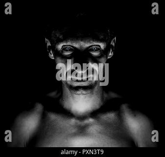 Foncé élégant portrait of caucasian homme qui regarde droit à vous et ressemble à ce maniaque. Yeux expressifs. Tourné en noir et blanc, d'éclairage low key. Banque D'Images