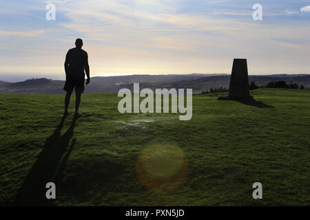 L'homme se découpant sur une colline à côté de trig point, avec lens flare Banque D'Images