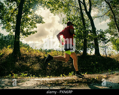 Coureur de l'homme pantalon short noir jaune et rouge t-shirt saute sur la piscine sur route asphaltée. Soirée fitnes exercice dans le parc automne Banque D'Images