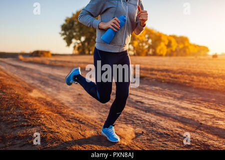 Femme d'exécution dans le champ d'automne au coucher du soleil. Concept de vie sain. Sportifs actifs. Close up de jambes