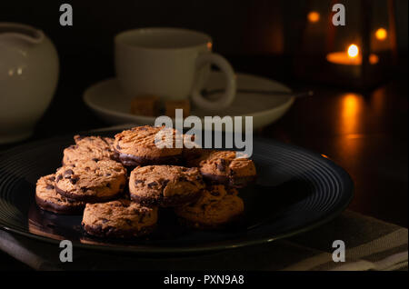 Cookies aux pépites de chocolat fait maison sur une table de cuisine avec du lait, chocolat noir et une tasse de café. Banque D'Images