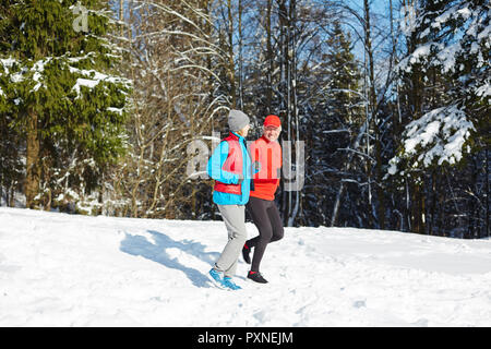 Senior conjoints ayant l'entraînement sportif sur l'hiver au chaud jour chez firtrees in snow Banque D'Images