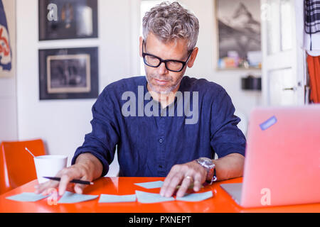 Homme mûr avec des blocs-notes et ordinateurs portables sur la table à la maison Banque D'Images