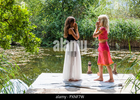 Deux filles debout face à face sur jetée à un étang en robes de fantaisie Banque D'Images