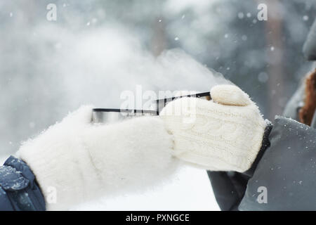Close-up of méconnaissable dans les campeurs mitaines blanc tasses et thermos holding toasting avec boisson chaude en hiver, ils debout sous la neige Banque D'Images