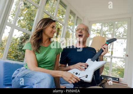 Mature Woman sitting on sofa at home with toy guitare électrique Banque D'Images