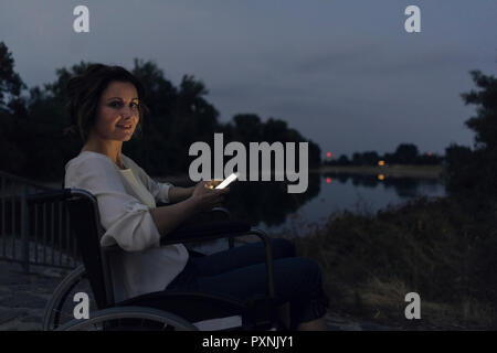 Mobilité woman sitting in wheelchair, using smartphone Banque D'Images