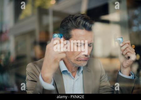 Mature businessman sitting in coffee shop, holding mini fans Banque D'Images