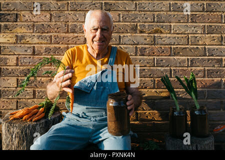 Smiling senior homme avec des pots de verre de terre et de carottes fraîches looking at camera Banque D'Images