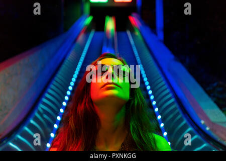 Portrait de jeune femme portant des lunettes de soleil lumineux en face de l'escalator bleus lumineux Banque D'Images