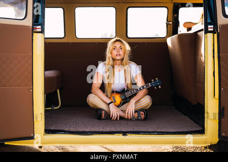 Jeune femme assise dans un van avec une guitare Banque D'Images