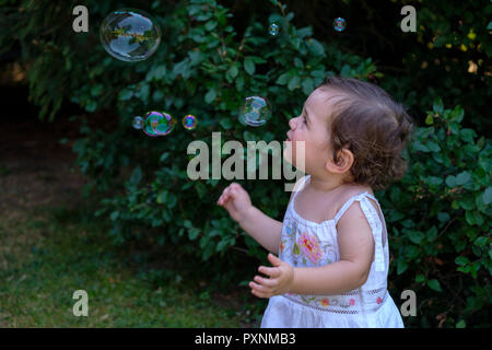 Baby Girl regarder voler des bulles de savon dans le jardin Banque D'Images