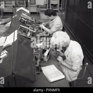 Années 1950, historiques, deux travailleurs féminins assis à un établi à l'aide d'équipements de soudage d'adhérer ou de brancher les fils sur les petits composants électriques utilisés dans l'industrie de l'aviation. Soudage utilise une substance contenant qui est flux conçus pour améliorer le contact électrique et mécanique dans les joints de soudure. Banque D'Images