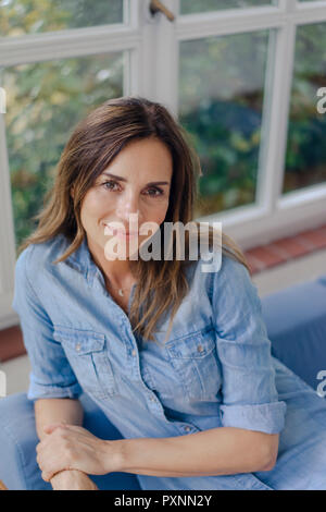 Portrait of smiling mature woman sitting on sofa at home Banque D'Images