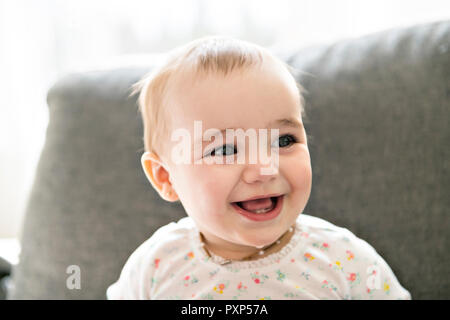 Un bébé souriant sur un canapé gris Banque D'Images