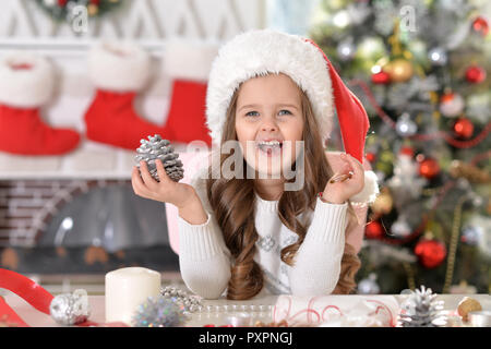 Portrait of happy little girl in Santa hat avec cône de pin decoration Banque D'Images