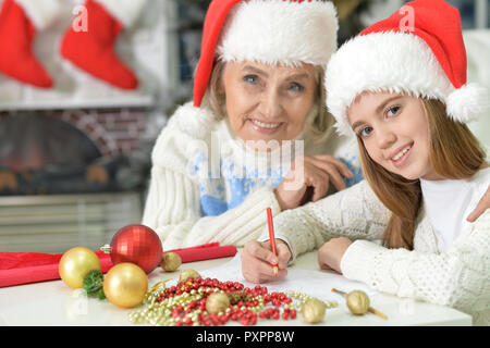 Portrait de grand-mère avec teen girl in Santa hats la préparation de Noël à la maison, fille lettre d'écriture Banque D'Images