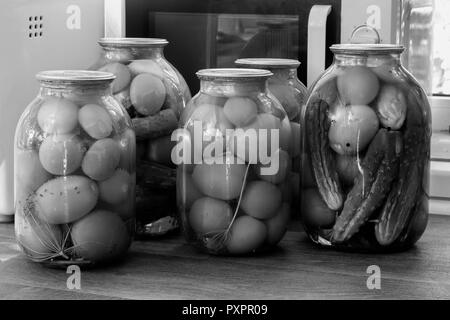 Accueil préservation : grands pots en verre rouge avec des tomates mûres et concombres, scellée. metallid Image noir et blanc. Banque D'Images